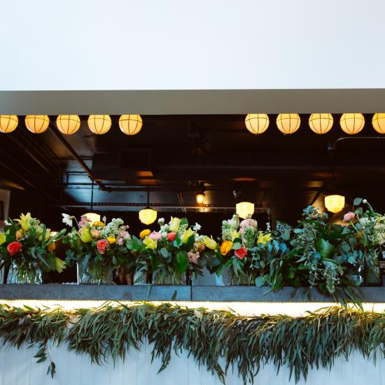 Garland under the bar with medium centerpieces in upgraded containers lined up and waiting for the flip